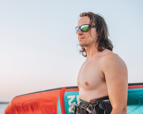 a surfer standing at the beach holding a surfing kite wearing Torege polarized sunglasses