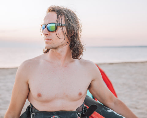 a man holding a surfkite wearing Torege polarized sunglasses standing by the beach